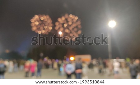 A crowd of people watch the city's nighttime fireworks display unfocused.