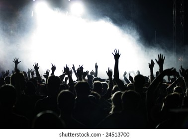Crowd raising hands at a pop concert;  white and grey-blue fog