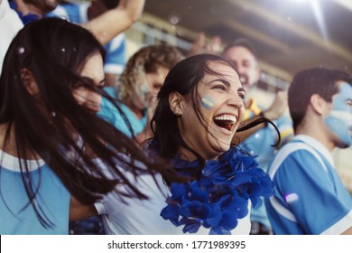 Crowd of sports fans of Argentina cheering during a match in stadium. Group of friends watching sports game celebrating when their team scoring a goal.