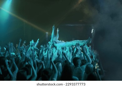 Crowd surf, blue light and people at concert or at music festival, lights and energy at live event. Dance, fun and group of excited fans in arena at rock show performance, group carrying fan on hands - Powered by Shutterstock