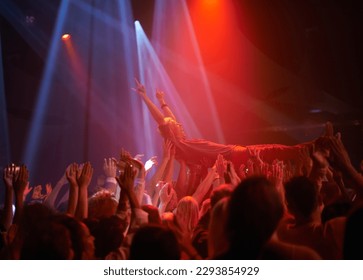 Crowd surf, light and people at music festival, neon lights and energy at live concert event. Dance, fun and group of excited fans in arena at rock show performance, audience carrying fan on hands. - Powered by Shutterstock