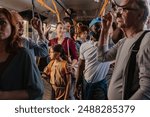 A crowded bus with diverse commuters standing and holding onto handrails during a busy ride.