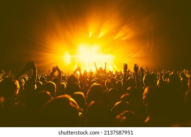 A crowded concert hall with scene stage orange and yellow lights, rock show performance, with people silhouette, colourful confetti explosion fired on dance floor air during a concert festival
 - Powered by Shutterstock