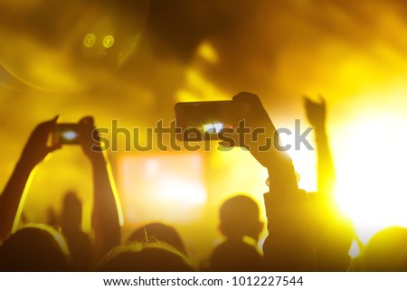 Crowds Enjoying Themselves At Music Festival, smartphone in hands during the rock concert, Raised hands