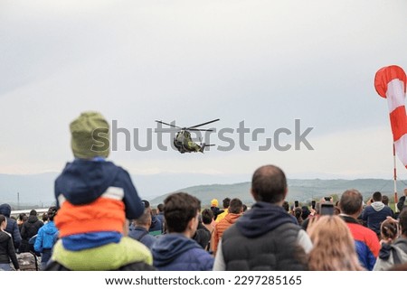 Crowds of people look at the military helicopter in flight. Air show.