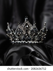 Crown for miss beauty, a symbol of power and elegance, competition, show. Tiara in white metal and black stones on a black draped satin background