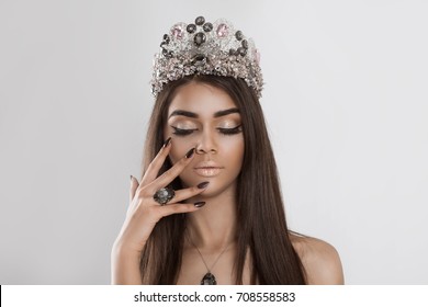 Crowned dark beauty queen. Fashion model girl woman beautiful shiny makeup eye shadow lipstick crystals set ring necklace crown looking down eyes closed showing velvet effect burgundy nails manicure