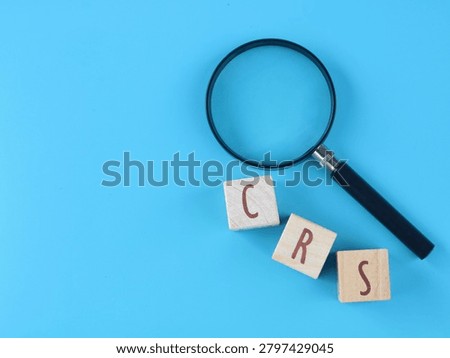 CRS (Common Reporting Standard) text on wooden blocks with magnifying glass against blue background. Represents financial transparency, international tax compliance, audit, and global information exchange regulations