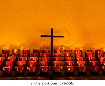 Crucifix And Red Candle Holders With Cross In Catholic Church Against Old Adobe Wall