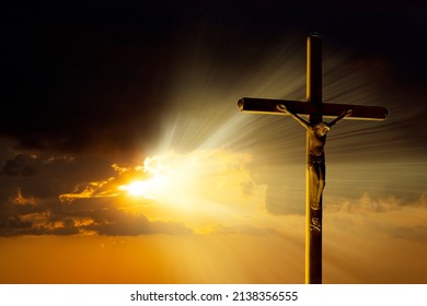 The crucifixion cross stands against the backdrop of an impressive golden sky with radiant rays penetrating through the clouds