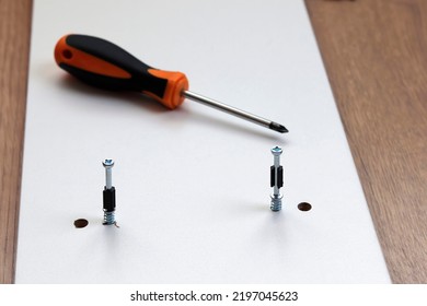 A cruciform screwdriver with a black and orange rubber handle and a partially screwed screw for furniture assembly - Shutterstock ID 2197045623