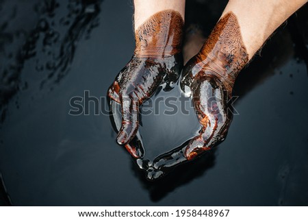 Crude oil in a bowl of hands on the background of a black oily puddle. The process of processing petroleum products. Folded cups of hands with fuel oil. Сrisis of the oil industry. Economic downturn.