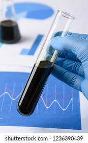 Crude Oil Sample In Scientist Hand In Laboratory. Fossil Fuel Charts On Background.