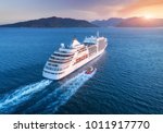 Cruise ship at harbor. Aerial view of beautiful large white ship at sunset. Colorful landscape with boats in marina bay, sea, colorful sky. Top view from drone of yacht. Luxury cruise. Floating liner