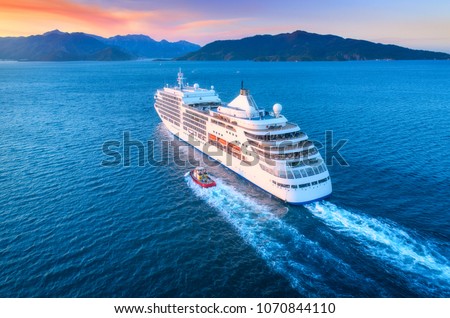 Cruise ship at harbor. Aerial view of beautiful large white ship at sunset. Colorful landscape with boats in marina bay, sea, colorful sky. Top view from drone of yacht. Luxury cruise. Floating liner