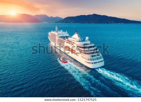 Cruise ship at harbor. Aerial view of beautiful\
large white ship at sunset. Colorful landscape with boats in marina\
bay, sea, colorful sky. Top view from drone of yacht. Luxury\
cruise. Floating liner