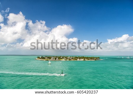 cruise touristic boats or yacht floating by island with houses and green trees on turquoise water and blue cloudy sky, yachting and isle life around beautiful Key West Florida, USA