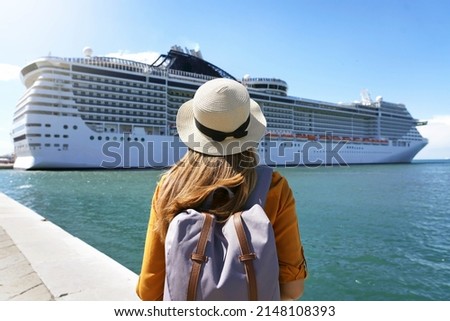 Cruise vacation. Rear view of tourist girl with backpack and hat standing in front of big cruise ship.