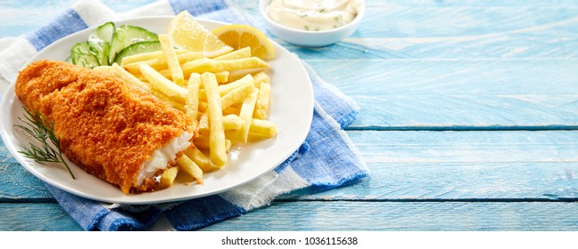 Crumbed deep fried fillet of cod served with potato chips and a cucumber salad on rustic blue wood in panorama banner format with copy space - Powered by Shutterstock