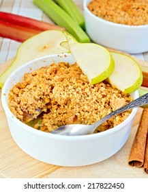 Crumble with pears and rhubarb in a white bowl on a wooden board, cinnamon on a background of striped linen tablecloth