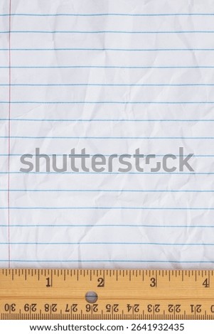 Crumbled lined loose leaf notebook paper with ruler background for schoolwork, measurement, education, or learning materials