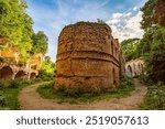 Crumbling brick walls of Tarakaniv Fort, an abandoned 19th-century fortress in Ukraine. Overgrown with vegetation, the circular tower stands amid dirt paths and arched structures.