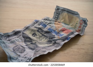 Crumpled $100 US dollar bill banknote on wooden table background. Global world economy recession crisis due to inflation, stagflation and FED control interest rates to GDP down soft landing concept.