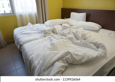 Crumpled Bed In The Hotel. Close-up Of Unfinished Or Messy Bed After Funny Night, Sex Of New Married Couple. Dirty Bed With Decorate Room. Used Linens, Bed Sheet And Pillows Messed Up.