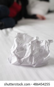 Crumpled Up Break Up Letter Sitting Discarded On A Bed With Woman In Background