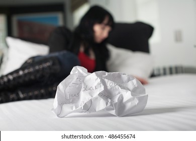 Crumpled Up Break Up Letter Sitting Discarded On A Bed With Woman In Background