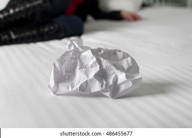 Crumpled Up Break Up Letter Sitting Discarded On A Bed With Woman In Background