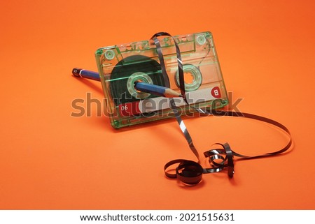 Crumpled cassette tape being rolled using blue pencil on isolated orange background                      