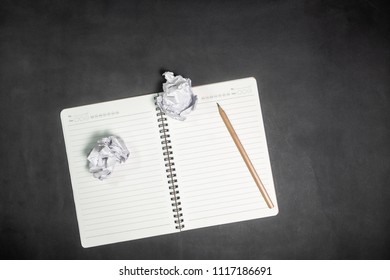 Crumpled paper ball and notebook on a black background.