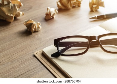 Crumpled Paper Balls With Eye Glasses And Notebook On Wood Desk With Soft Light