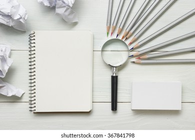 crumpled paper balls, magnifying glass, pencils and notebook with blank white sheet  on wooden table. Creativity crisis concept - Shutterstock ID 367841798