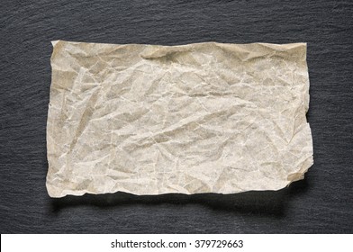 Crumpled paper sheet on black slate stone with copy space for text as template food background. Top flat view. Concept