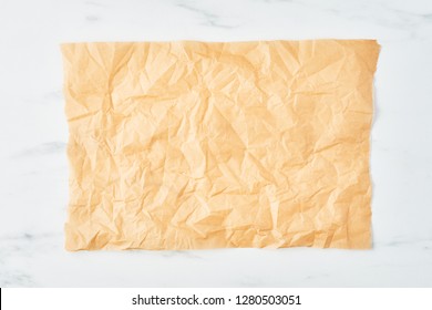 Crumpled piece of parchment or baking paper on white marble table. Top view. Copy space for text and design element.