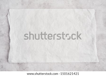 Crumpled piece of white parchment or baking paper on grey concrete background. Top view. Copy space for text and design element.