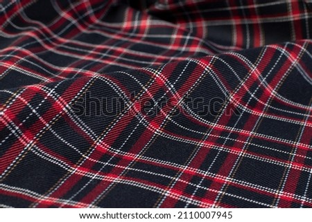 Crumpled red and black knitted plaid. The soft and warm fabric was crumpled in folds. Texture for the background. View from above