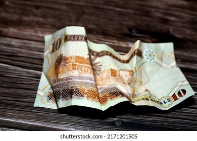 Crumpled Saudi Arabia money of 10 SAR ten riyals isolated on wooden background, wrinkled 10 Saudi Riyals cash bill banknote, Saudi money inflation and economy world crisis concept, selective focus