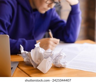 Crumpled sheets of paper in the background, a woman writes with a pen on paper. A writer or a student, a laptop on the table, a bad idea, a failure. Failed business plan - Powered by Shutterstock