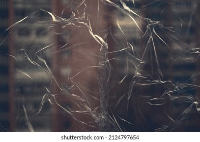 Crumpled transparent plastic film on the window glass on the background of buildings, polyethylene background, crumpled polyethylene on the window, polyethylene texture, grunge background