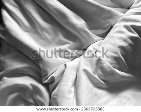 Crumpled white cotton bed sheet in soft and calm atmosphere of all white bed room, close up.