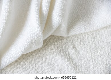 Crumpled white cotton shower or bath towel is thrown on a hotel bed after use. Towel is a thick fluffy absorbent cloth used for drying oneself or wiping things dry, usually made of 100 percent cotton.
