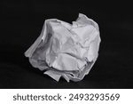 A crumpled white paper ball against a dark background. The image highlights the textures and folds of the paper, symbolizing waste, mistakes, or recycling.