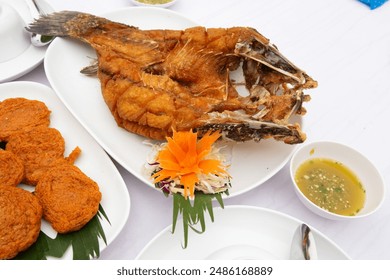 Crunch fried fish on white plate decorated with sliced carrot,cabbage and banana leaves,nearby a cup of seafood ketchup and on white background,close up image. - Powered by Shutterstock