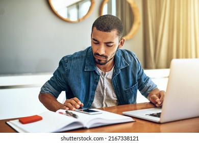 Crunching the numbers. Shot of a focused young man working on his laptop and checking his phone while being seated at a table at home. - Shutterstock ID 2167338121