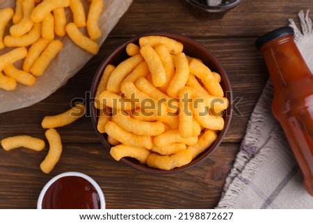 Crunchy cheesy corn snack and ketchup on wooden table, flat lay