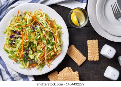 Crunchy Coleslaw Of Red And White Shredded Cabbage, With Carrot And Spring Onion With Oil And Lemon Dressing On A White Plate, With A Glass Of Water With Lemon, On A Wooden Table, Top View, Close-up