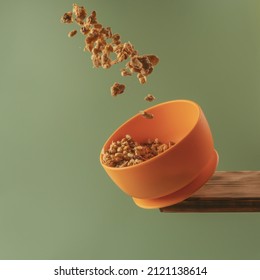 Crunchy granola flying out of modern orange silicone bowl with suction base standing on wooden board on green background. Serving food, baby tableware, feeding concept. Instagram use, square frame. - Shutterstock ID 2121138614